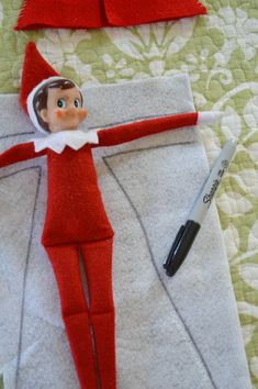 an elf doll laying on top of a bed next to a pen and paper towel