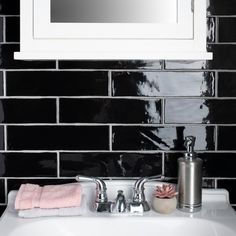 a white sink sitting under a mirror next to a black tiled bathroom wall with pink towels