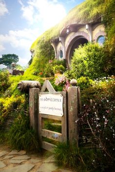 the hobbot house is surrounded by lush green plants and flowers, with a sign in front