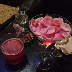 two wine glasses with flowers in them on a table next to another glass filled with liquid