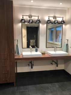 two sinks and mirrors in a bathroom with lights on the wall above them, along with dark tile flooring