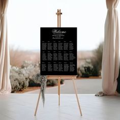 an easel with a welcome sign on it in front of a window and curtains