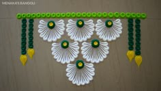 a wall hanging made out of white and green beads on a wooden surface with yellow accents