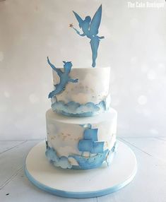 a three tiered cake with blue icing and flying birds on top, sitting on a white plate