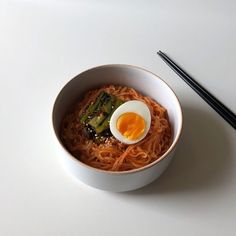 a bowl of noodles with an egg on top and chopsticks next to it