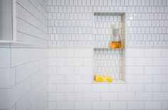 a white tiled bathroom with two bottles of orange juice on the shelf next to it