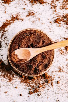 a wooden spoon sitting in a bowl filled with cocoa powder and ground cinnamon on a white surface