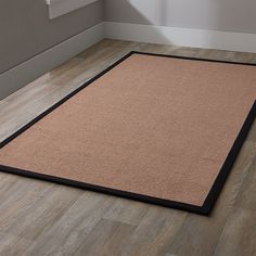 a beige area rug with black border on the floor in front of a white wall