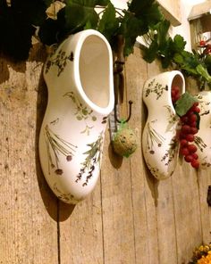 three white vases are hanging on a wooden wall with grapes and other flowers around them