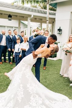 a bride and groom kissing in front of their wedding party on the lawn at an outdoor venue