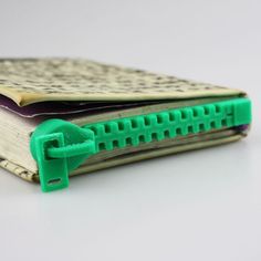 an open book with green plastic clips on the front and back cover, sitting on a white surface