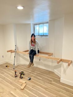 a woman sitting on top of a wooden bench in a room with hard wood flooring