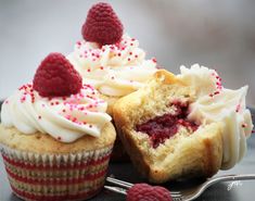 two cupcakes with white frosting and raspberries on top