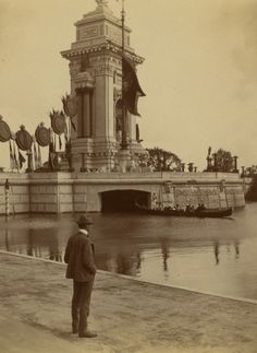 an old photo of a man standing in front of a building next to the water