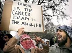 two men holding up signs and wearing scarves on their heads while standing in front of a crowd