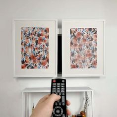 a person holding a remote control in front of two pictures on the wall above them