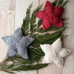 three knitted star ornaments sitting on top of a wooden table next to pine branches