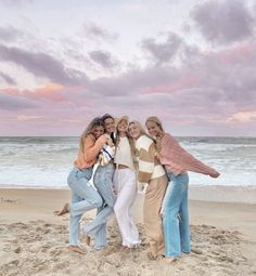 four women standing together on the beach at sunset