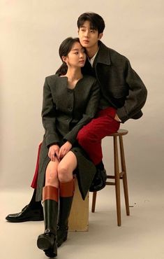 a man and woman sitting next to each other on top of a wooden stool in front of a white wall