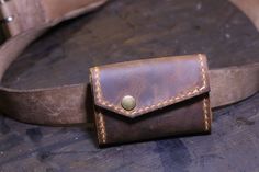 a brown leather wallet sitting on top of a piece of wood next to a belt