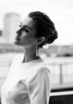 black and white photo of woman in dress looking off to the side with cityscape in background