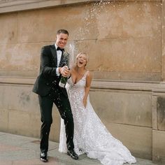 a bride and groom standing in front of a fountain spraying champagne into the air with their hands