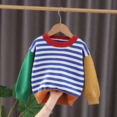 a person holding up a striped sweater on a clothes line with a plant in the background