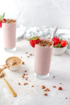 two glasses filled with smoothie topped with strawberries and granola on a white table