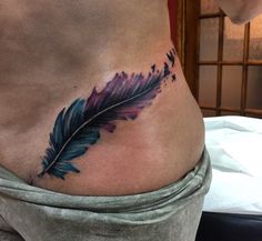 a woman's stomach with a feather tattoo on her side and the bottom part of her belly