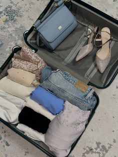 an open suitcase filled with clothes and shoes on the floor next to a handbag