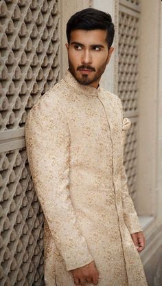 a man standing next to a wall wearing a white suit