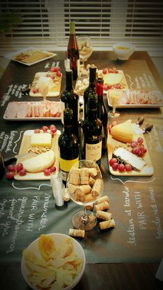 a table topped with lots of wine bottles and plates filled with cheese, crackers and grapes