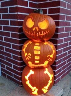 three carved pumpkins sitting on top of each other in front of a brick wall