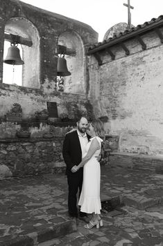 a man and woman standing next to each other in front of an old brick building