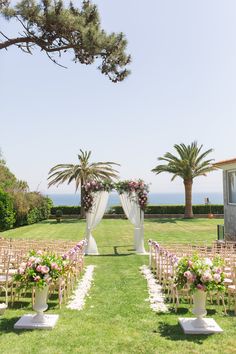 an outdoor ceremony set up with chairs and flowers on the aisle, overlooking the ocean