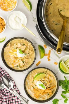 three bowls of soup with tortilla chips, sour cream and limes on the side