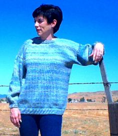 a woman standing in front of a fence with her hand on her hip and looking off to the side