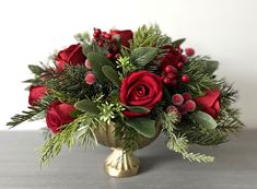 a bouquet of red roses and greenery in a gold vase on a gray surface