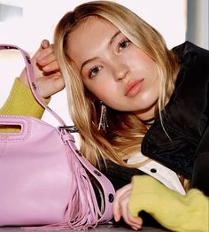 a woman holding a pink handbag next to her face and looking at the camera