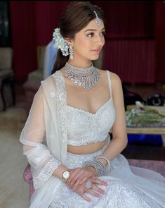 a woman in a white dress sitting on a pink couch wearing jewelry and bracelets