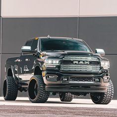 a black ram truck parked in front of a building with large tires on it's wheels