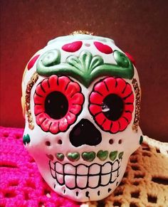 a white skull with red and green flowers on it's face sitting on a table