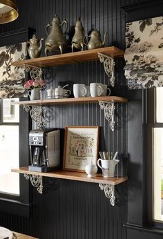 a kitchen with black walls and shelves filled with coffee cups, tea kettles and other items