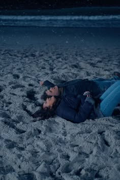 a man and woman laying on the beach in the sand at night with their eyes closed