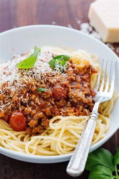 a plate of spaghetti with meat sauce and parmesan cheese on the side next to some bread