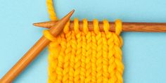 an orange knitted piece with two wooden needles next to it on a blue surface