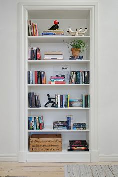 a bookshelf filled with lots of books next to a white wall