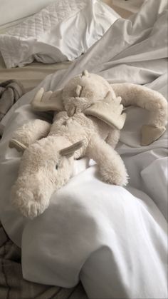 a white stuffed animal laying on top of a bed covered in sheets and blankets,