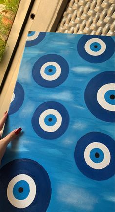 a hand is holding up a piece of paper with circles painted on it, and the background is blue