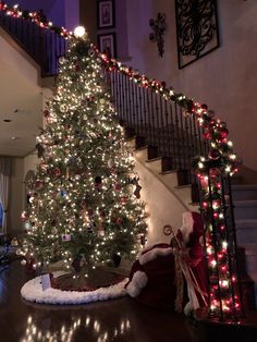 a decorated christmas tree in the corner of a living room with stairs and railings